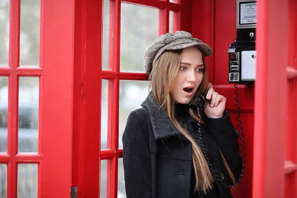 Menina bonita em uma cabine telefônica. A menina está falando no th — Fotografia de Stock