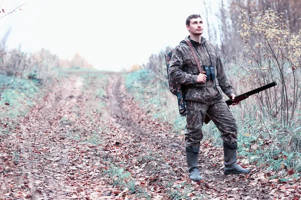 Un homme en camouflage et avec un fusil de chasse dans une forêt sur une espèce — Photo