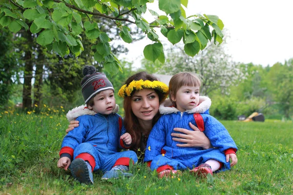 Madre con gemelli giovani seduti su un prato verde all'inizio di sprin — Foto Stock