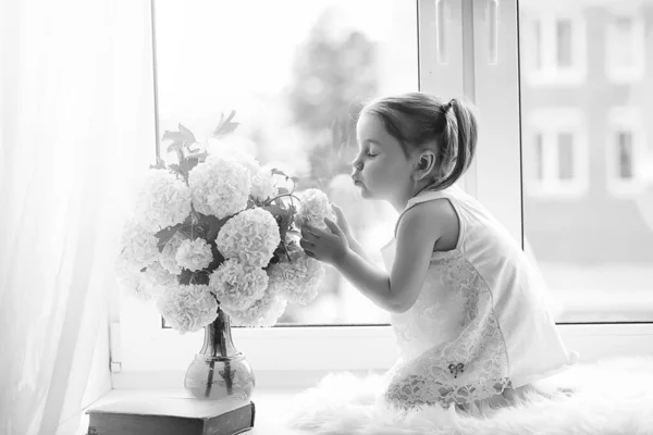 Una niña está sentada en el alféizar de la ventana. Un ramo de flores —  Fotos de Stock