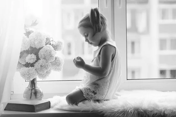 Malá holka sedí na okenním parapetu. Kytice květiny — Stock fotografie