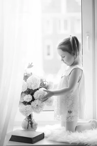 Una bambina è seduta sul davanzale della finestra. Un mazzo di fiori — Foto Stock