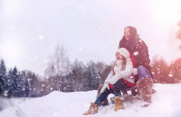 En vintersaga, en ung mamma och hennes dotter rida en släde — Stockfoto