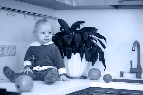 Foto monocromática de un niño pequeño en la cocina se sienta en una mesa — Foto de Stock