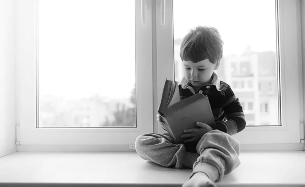 A kisfiú egy könyvet olvas. A gyerek ül az ablakban a — Stock Fotó