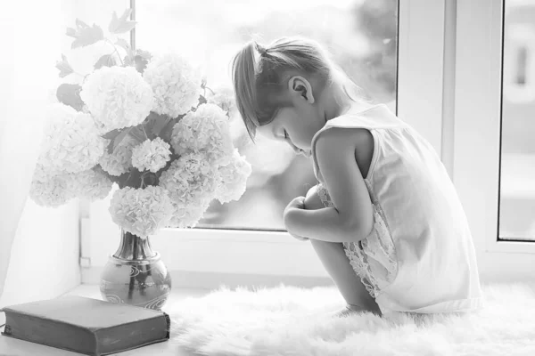 Una niña está sentada en el alféizar de la ventana. Un ramo de flores —  Fotos de Stock