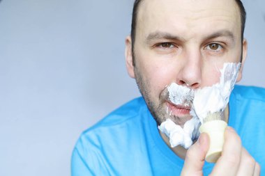 Bir adam aynanın önünde tıraş olur. Tıraş köpüğü. Tek kullanımlık jilet..