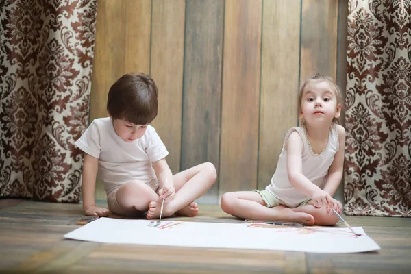 Niños pequeños pintan en una hoja grande de papel —  Fotos de Stock