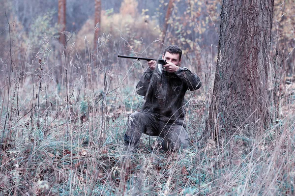 Um homem em camuflagem e com uma espingarda de caça em uma floresta em uma sp — Fotografia de Stock
