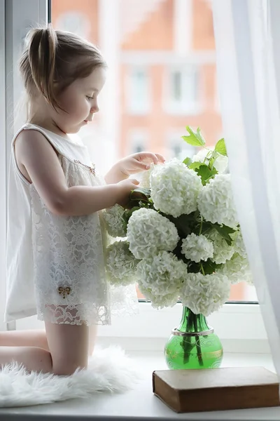 一个小女孩正坐在窗台上。一束鲜花 — 图库照片