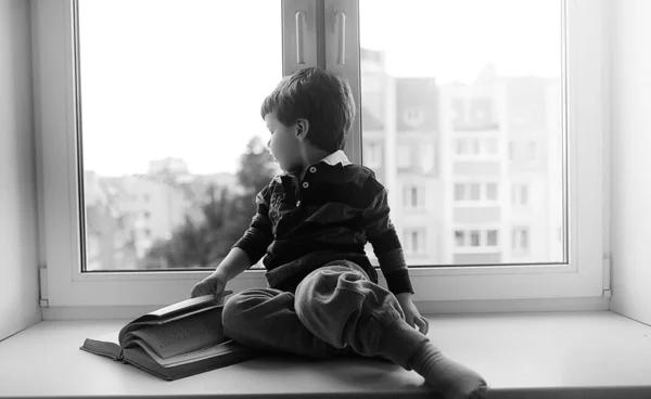 El niño está leyendo un libro. El niño se sienta en la ventana a —  Fotos de Stock