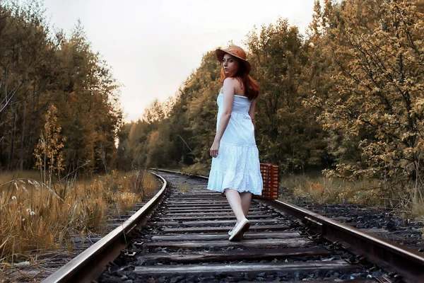 Chica del parque de otoño en vestido blanco y una maleta de mimbre caminando — Foto de Stock