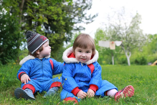 Mutter mit kleinen Zwillingen sitzt im Frühfrühling auf einer grünen Wiese — Stockfoto