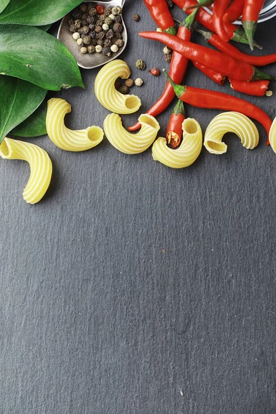 Uncooked pasta on a stone background. With seasonings and spices