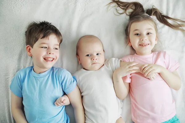 Barnen ligger på sängen bredvid det nyfödda barnet, lillasyster. — Stockfoto