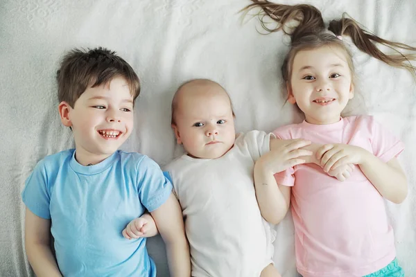 Children lie on the bed next to the newborn baby, little sister. — Stock Photo, Image