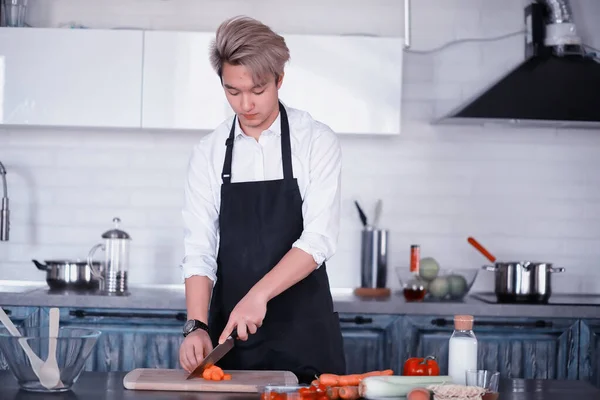 Asian cook in the kitchen prepares food in a cook suit — Stock Photo, Image