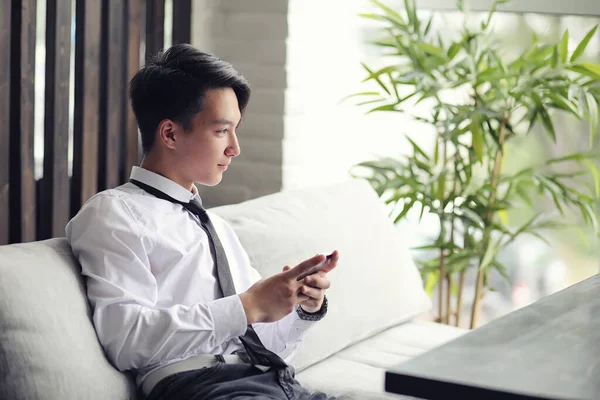 A young Asian businessman is waiting for a partner in a cafe. Bu — Stock Photo, Image