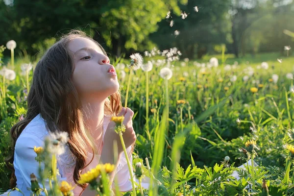 Remaja meniup biji dari bunga dandelion di taman musim semi — Stok Foto