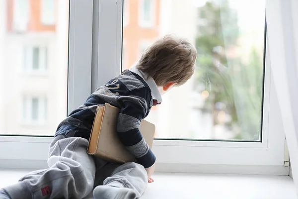 The little boy is reading a book. The child sits at the window a — Stock Photo, Image