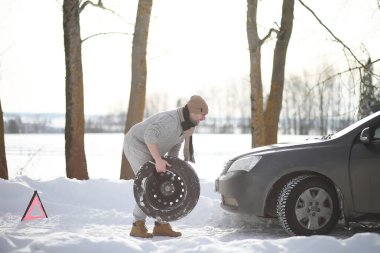 Bir adamın yanında bir kış gününde kırık bir araba