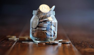 Ahşap bir zemindeki cam kavanozdaki bozuk paralar. Bozuk paradan cep tasarrufu