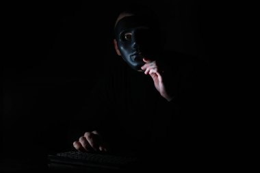 Maskeli bir adam karanlıkta klavyeye baskı yapmış.