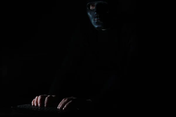 Um homem com uma máscara imprime no teclado no escuro — Fotografia de Stock