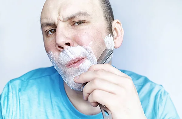 Mężczyzna goli się przed lustrem. Pianka do golenia. Brzytwa jednorazowego użytku. — Zdjęcie stockowe