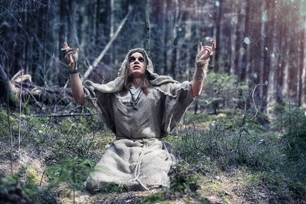 Een man in een soutane besteedt een ritueel in een donker bos — Stockfoto