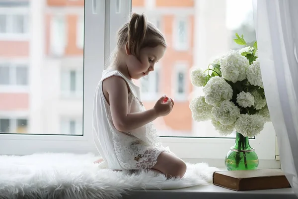 Malá holka sedí na okenním parapetu. Kytice květiny — Stock fotografie