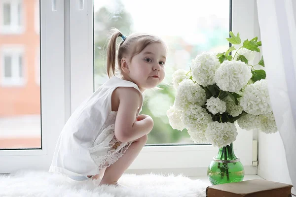 A little girl is sitting on the windowsill. A bouquet of flowers — Stock Photo, Image