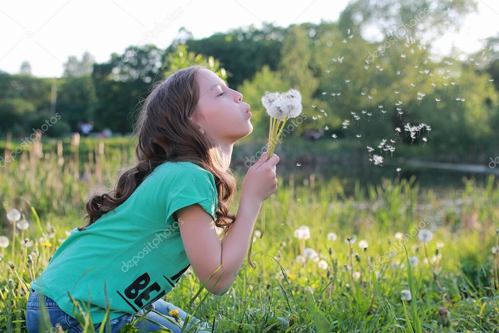 Teen blowing seeds from a dandelion flower in a spring park