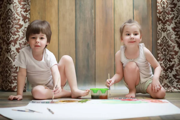 Niños pequeños pintan en una hoja grande de papel —  Fotos de Stock