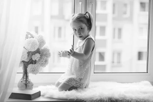 Mała dziewczynka siedzi na parapecie. Bukiet kwiatów — Zdjęcie stockowe