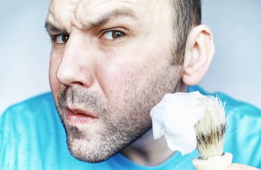 Bir adam aynanın önünde tıraş olur. Tıraş köpüğü. Tek kullanımlık jilet..