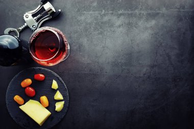 Şarap kadehi ve siyah şarap şişesi. Ceviz peyniri ve domates.