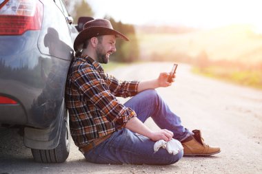 Adam yolda arabanın yanında oturuyor