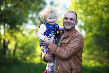 Güneşli bir günün akşamında babasıyla parkta bir kız.