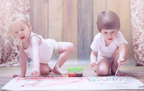 Niños pequeños pintan en una hoja grande de papel — Foto de Stock