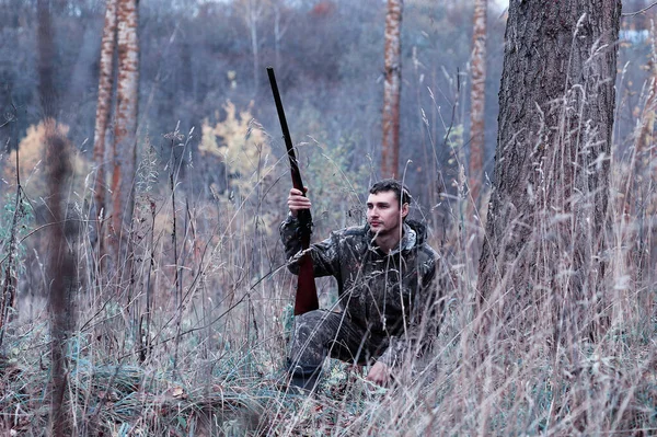 Un homme en camouflage et avec un fusil de chasse dans une forêt sur une espèce — Photo