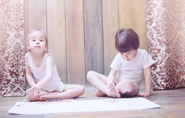 Niños pequeños pintan en una hoja grande de papel — Foto de Stock