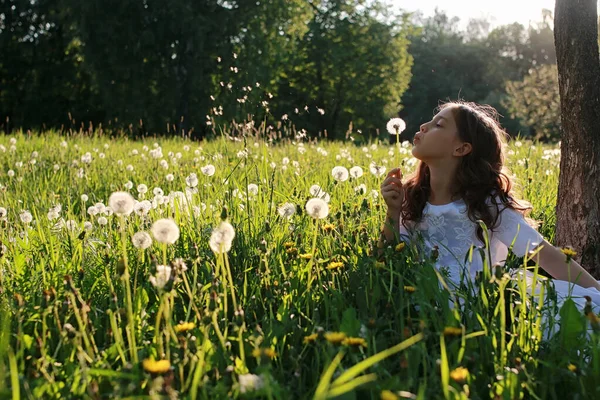 Adolescente soplando semillas de una flor de diente de león en un parque de primavera — Foto de Stock