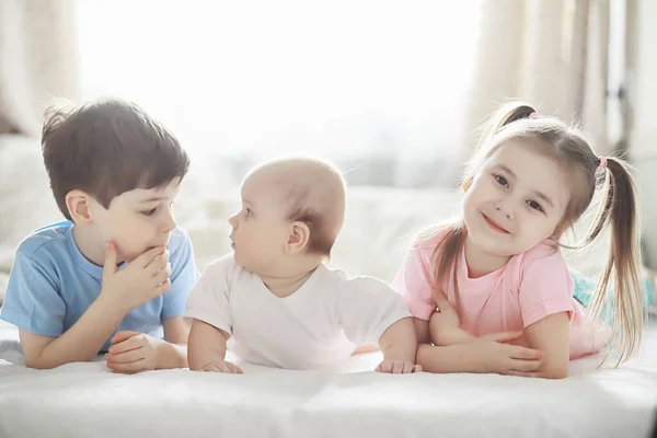 Kinderen liggen op het bed naast de pasgeboren baby, zusje. — Stockfoto