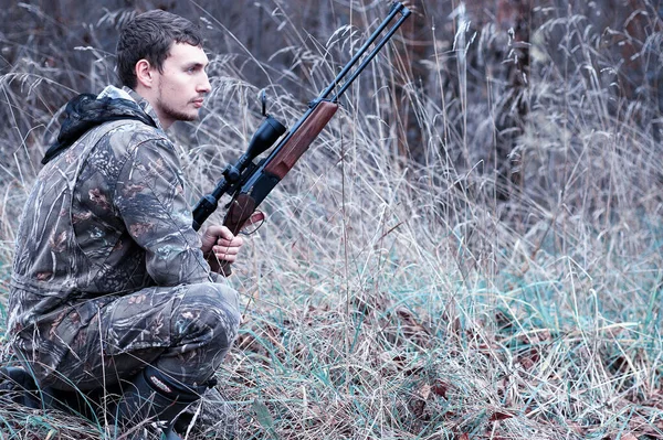 Muž v maskování a s loveckou puškou v lese na sp — Stock fotografie