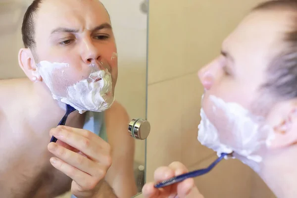 Um homem faz a barba na casa de banho pela manhã — Fotografia de Stock