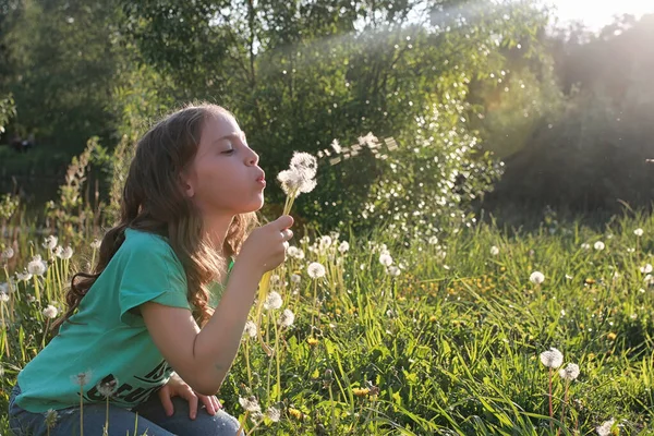 Teen blowing seeds from a dandelion flower in a spring park — Stock Photo, Image