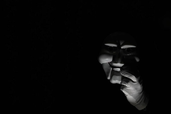White scary mask on a black background with whites hand.