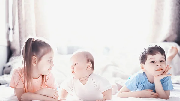 Kinderen liggen op het bed naast de pasgeboren baby, zusje. — Stockfoto