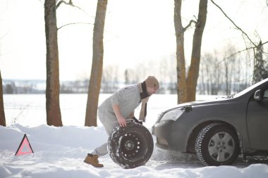 Bir adamın yanında bir kış gününde kırık bir araba